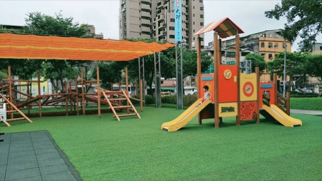 和平青草園的組合遊具，橘色遮陽帆下有木造攀爬架與黃色溜滑梯。