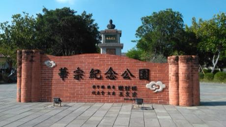 公園入口的紅磚弧形景觀牆，牆面有「華宗紀念公園」字樣與雲紋裝飾；後方為樹木與一座石造紀念碑，前方是石板廣場。
