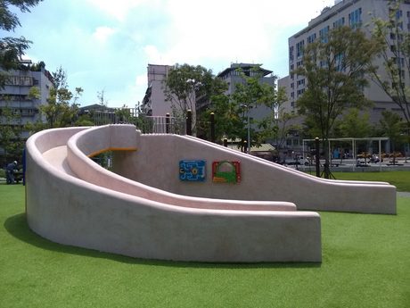 景勤1號公園的弧形磨石子滑梯土丘，兩道滑道之間有彩色遊戲面板，四周是人工草皮。