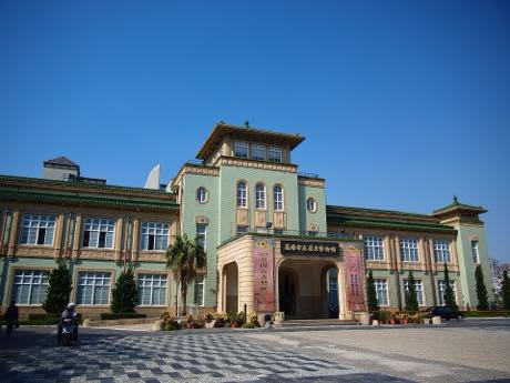 淺綠色外牆的歷史建築，中央為方形塔樓與拱形門廊，兩翼為對稱的兩層樓體與方窗；門前有盆栽與石板廣場。