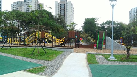 林口小熊公園的大型木構攀爬遊戲組，黃色攀爬網與木質斜坡設於木屑鋪面上，背景為林口重劃區住宅大樓。