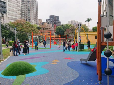 馬公公園小小航海家遊戲場，藍色海洋圖案的地墊上有溜滑梯和橘色滑索架，遠處有遊客。