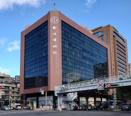 郵政博物館總館的粉褐色轉角建築，立面上方有紅色中華郵政標誌與直式「郵政博物館」字樣。