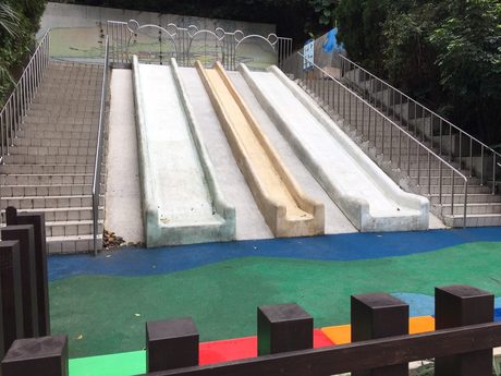 三峽中山公園山坡上的三道磨石子滑梯，兩側為階梯與扶手，下方是藍綠色波浪防護鋪面。