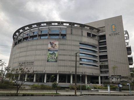 國立臺灣科學教育館的圓弧形館舍，灰色帷幕與水平帶窗環繞圓形主體，側翼有藍色 NTSEC 標誌。
