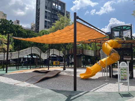 北屯兒童公園內橙色遮陽帆布下的黃色滾筒溜滑梯與繩網攀爬設施。