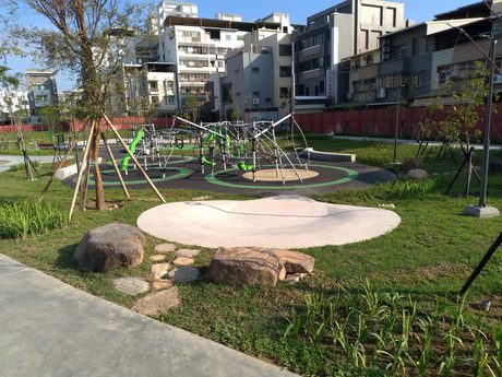 大元公園的攀爬網遊具與圓形鋪面，前方草地上有石塊與磨石子圓台。