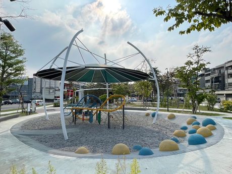 十全公園深綠色傘狀遮棚下的藍黃色攀爬繩網與溜滑梯遊具，地面鋪碎石與軟墊圓球。