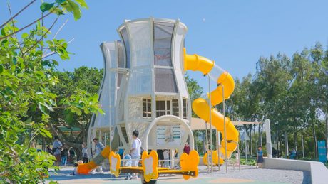 后里環保公園孩籽世界遊戲場的白色繭型攀爬塔與黃色螺旋滑梯，家長與小孩在旁遊玩。