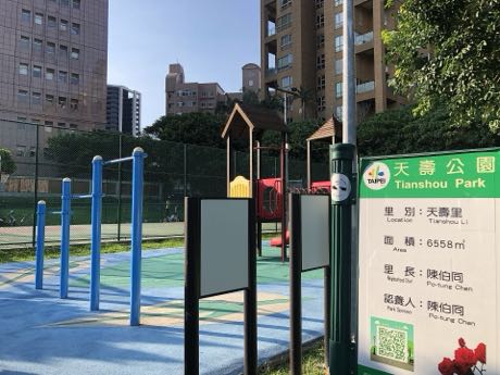 社區公園的兒童遊戲場與體健設施，設有攀爬架、單槓與彩色地墊；右側立有綠色公園資訊牌，標示公園名稱、面積與管理資訊，背景為住宅大樓。