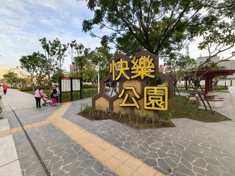 新莊快樂公園入口的蜂巢造型黃色招牌寫著「快樂公園」，旁邊是石板步道和樹木。