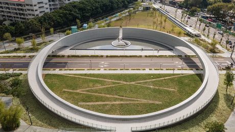 空拍1895乙未保台紀念公園，巨大的白色環形跨橋橫跨道路，圍住一邊的草坪與另一邊的紀念碑水池。